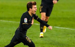 Riqui Puig comemora seu primeiro gol pelo Barça correndo, com a mão direita no escudo da camisa.