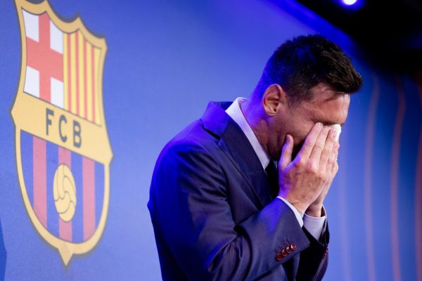 Messi, chorando, com as mãos no rosto. Atrás, um escudo do FC Barcelona. 